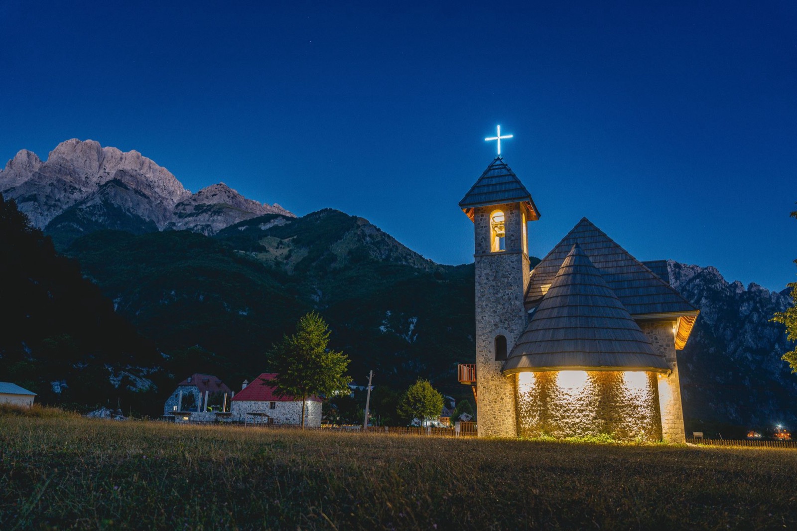 A lit stone church below sharp limestone peaks in the blue light after sunset