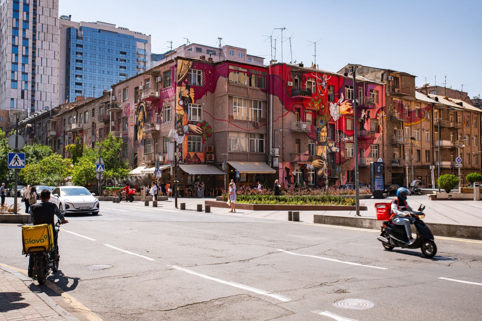 A large mural covering the facade of an old apartment block on a wide city street