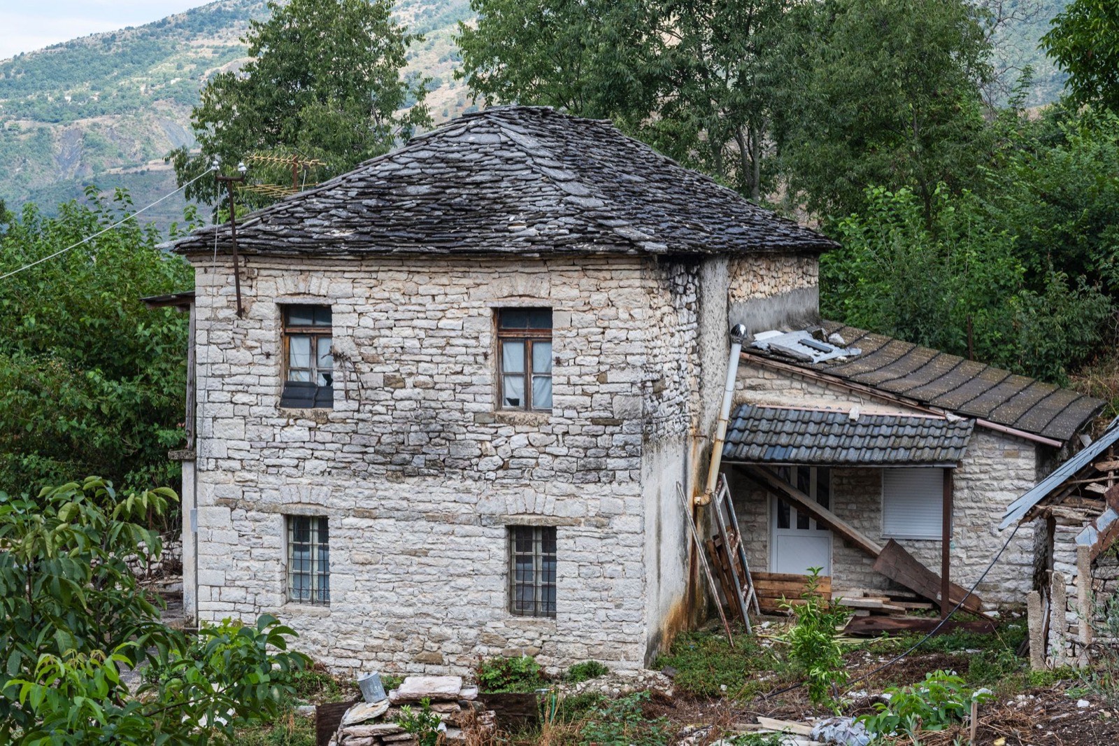 A stone house with a slate roof and outbuildings on a green hillside