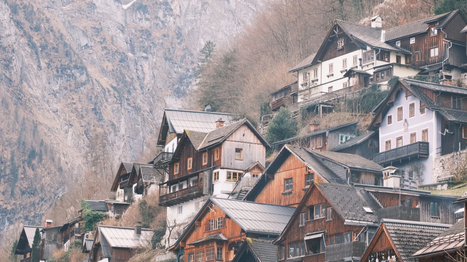 Wooden houses stacked up a steep slope below a grey cliff face in winter