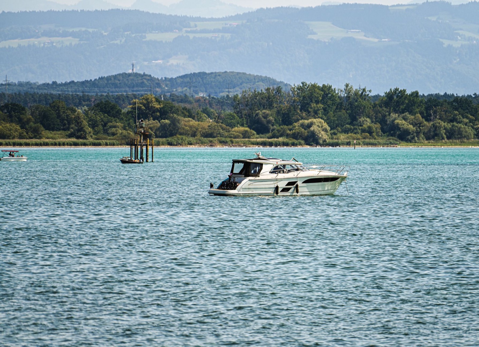 A motor boat on a wide lake with a wooded shore and low hills behind it