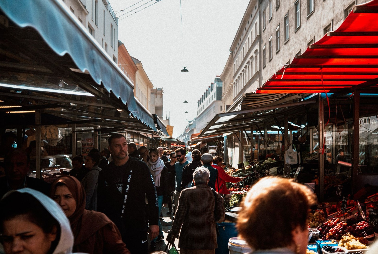 A crowded market lane between awning-covered stalls, with fruit and vegetables piled on the right