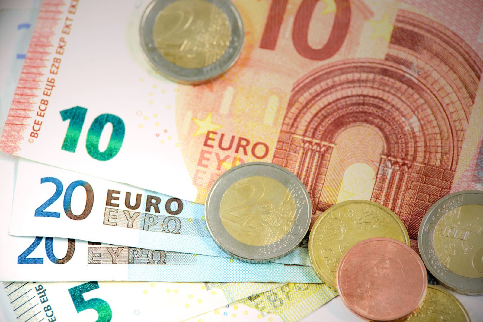 Five, ten and twenty euro notes fanned out with two euro and cent coins lying on top