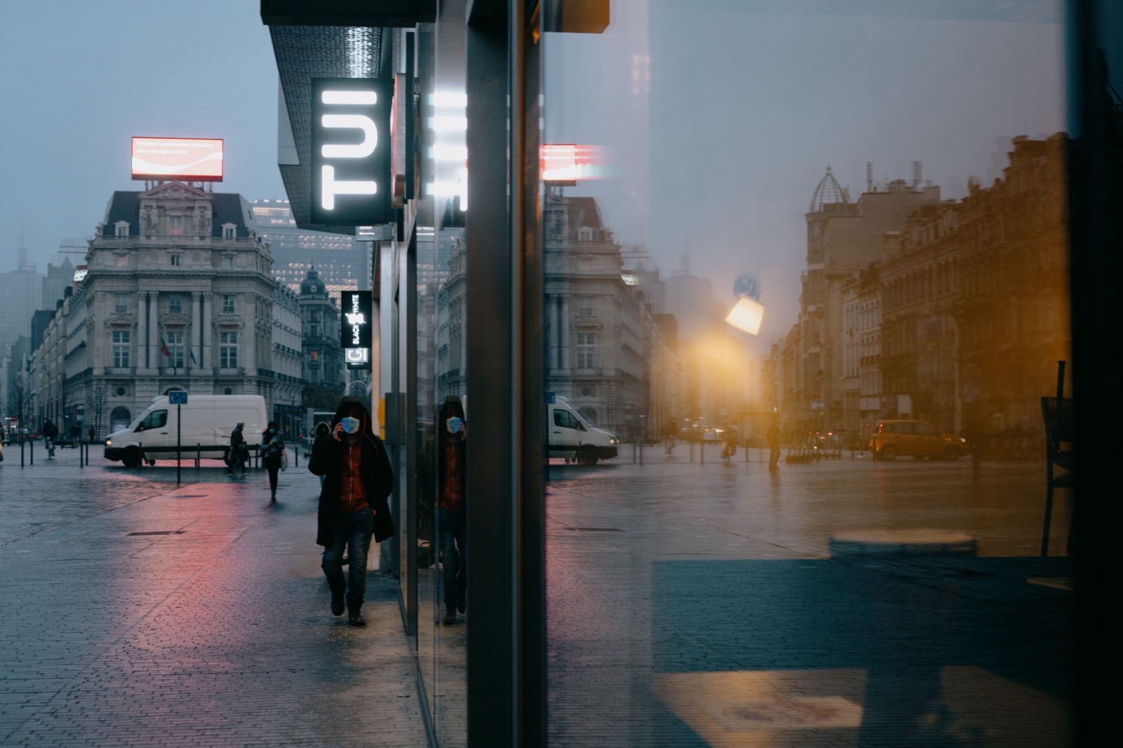 A rainy Brussels boulevard at dusk seen past a lit bus shelter