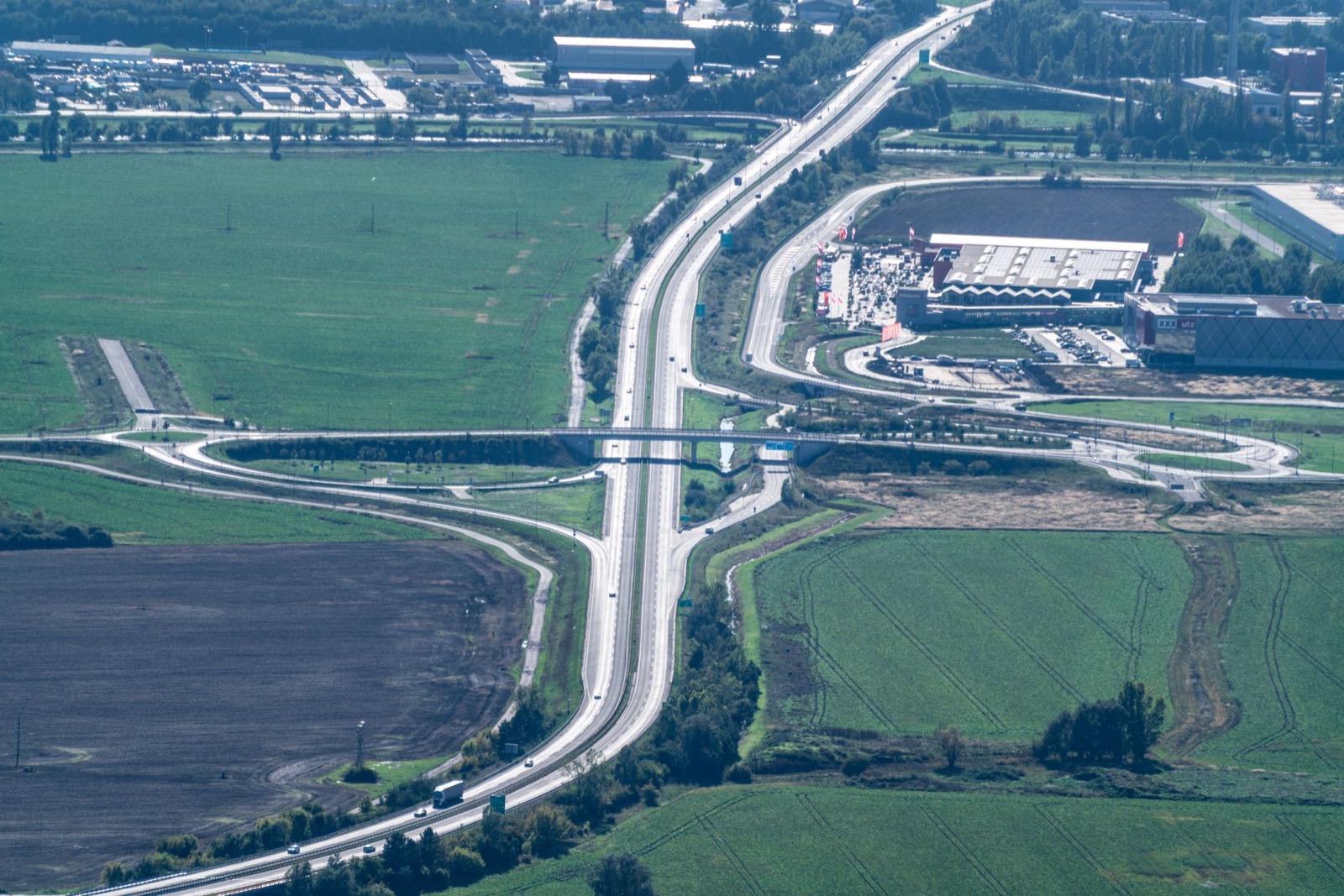 A motorway junction seen from the air, cutting between ploughed fields and green farmland