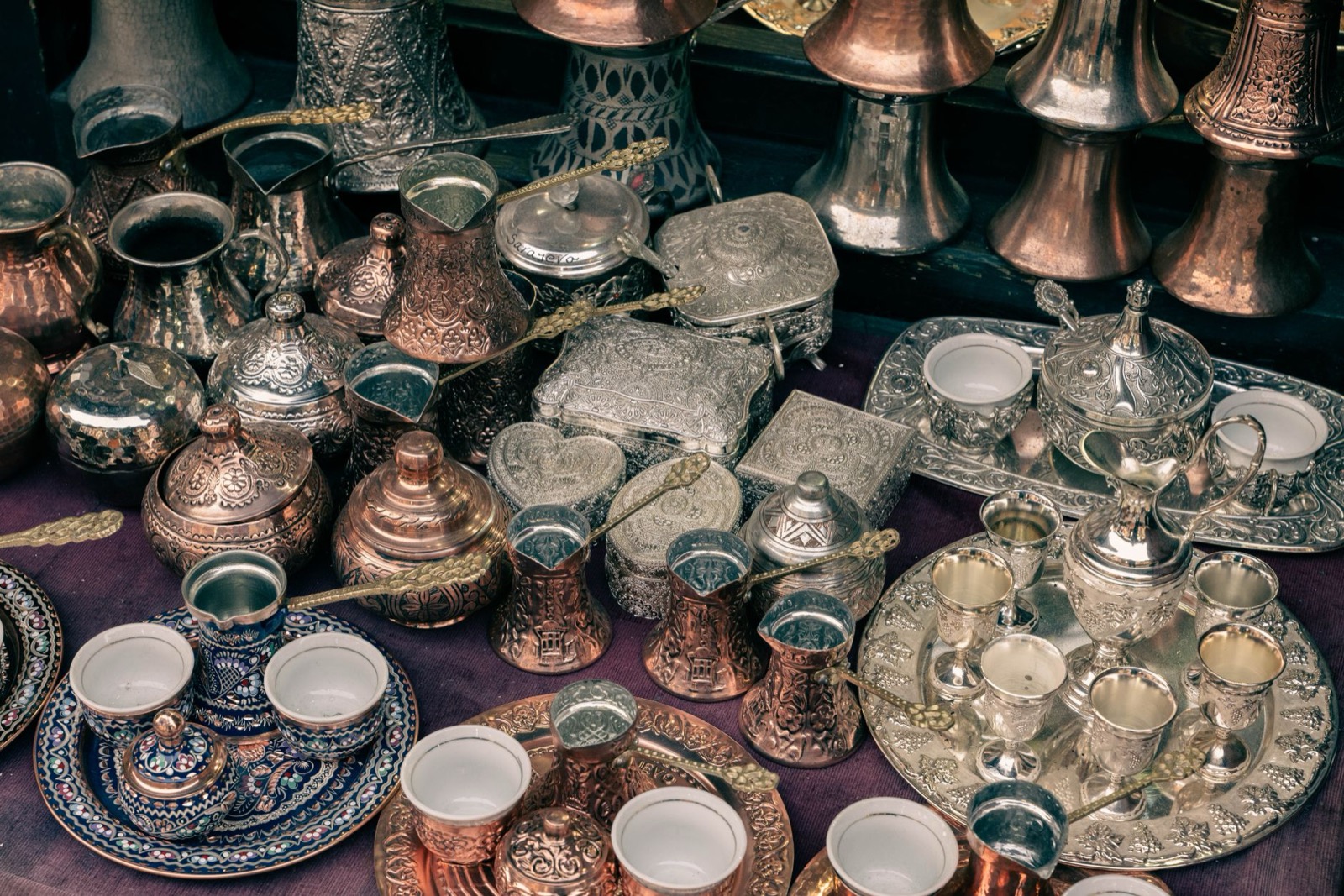 Engraved copper and silver coffee sets, long-handled pots and trays crowded on a market stall