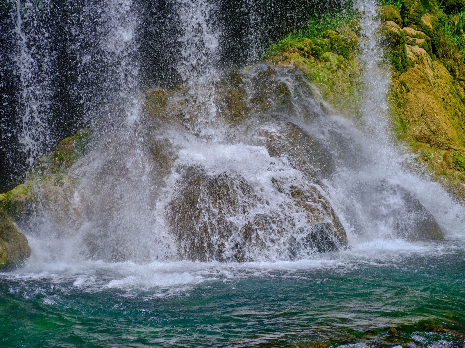 Water falling in sheets over a mossy rock into a turquoise pool