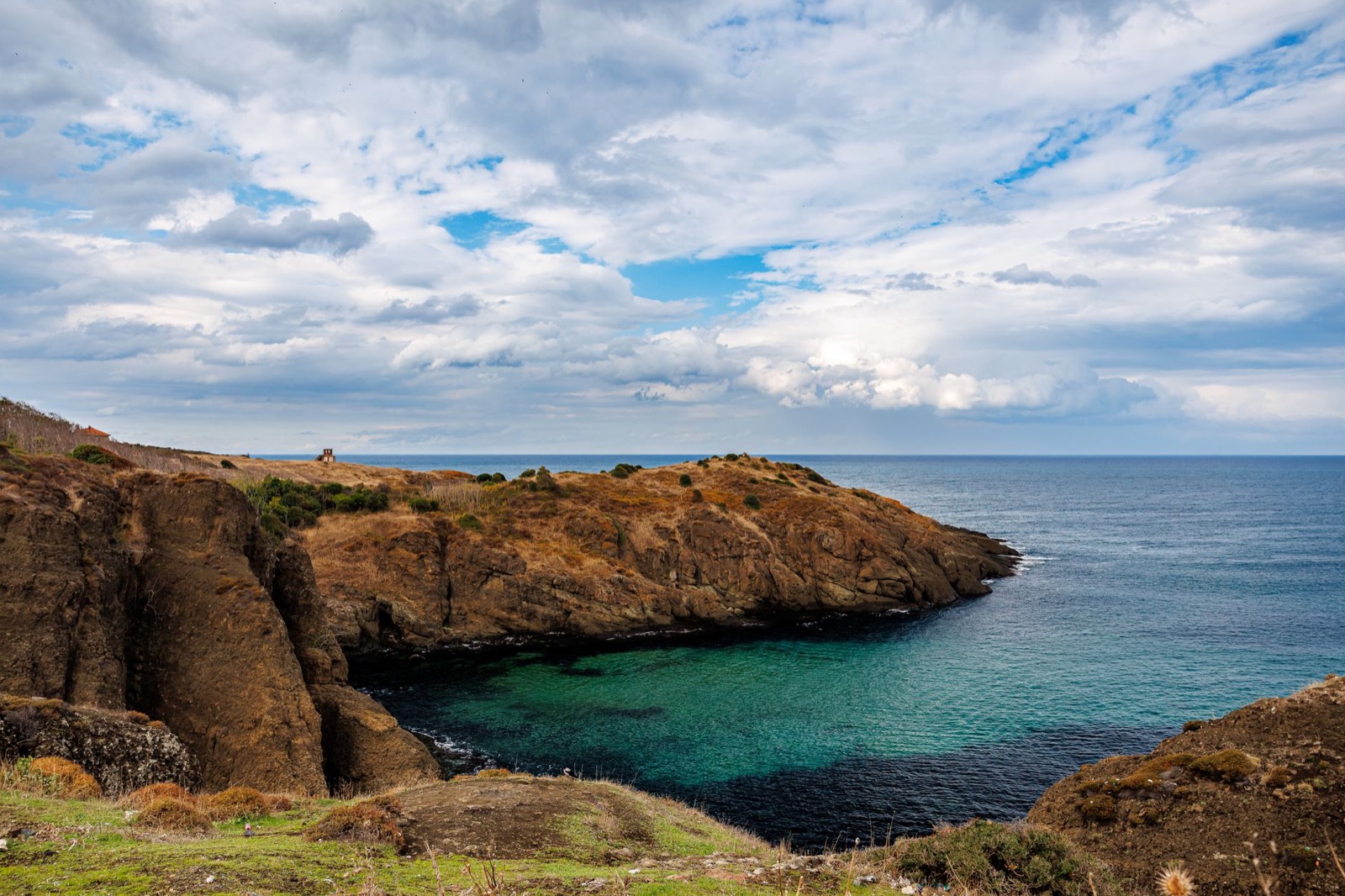 A turquoise cove enclosed by low brown cliffs under a cloudy sky