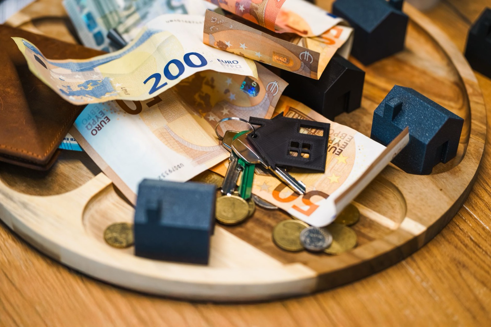 Euro banknotes, coins and a bunch of keys on a wooden tray with small model houses