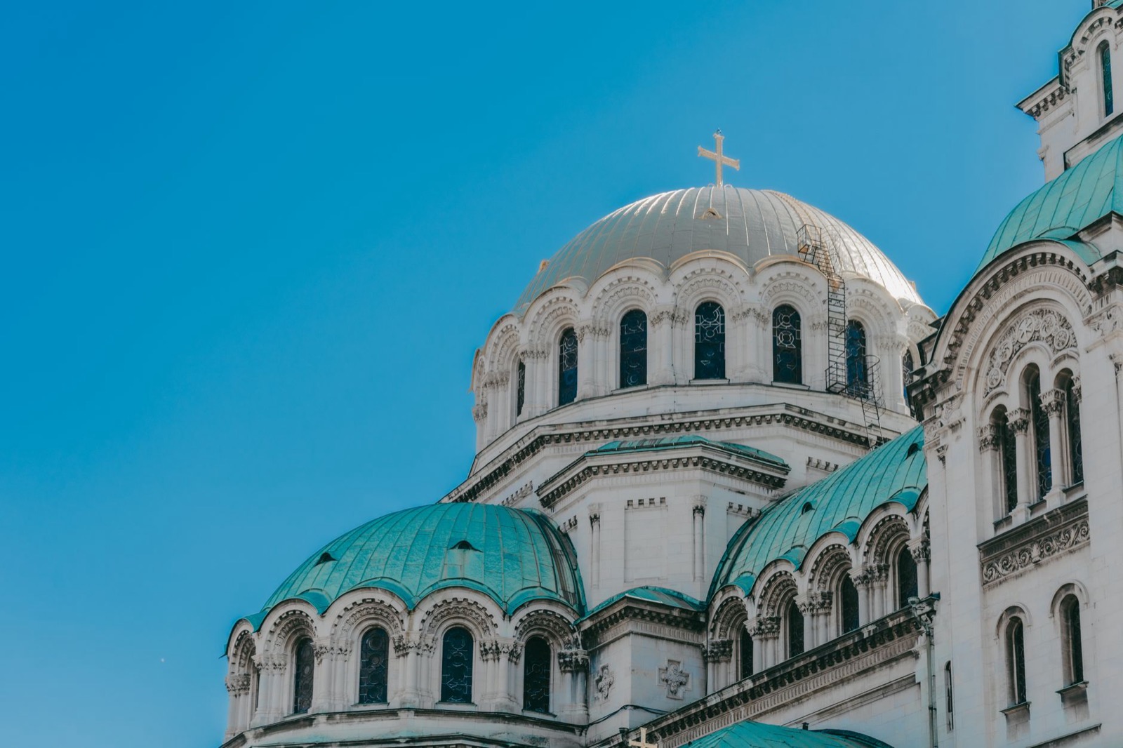 The green and pale domes of the Alexander Nevsky cathedral against a clear blue sky