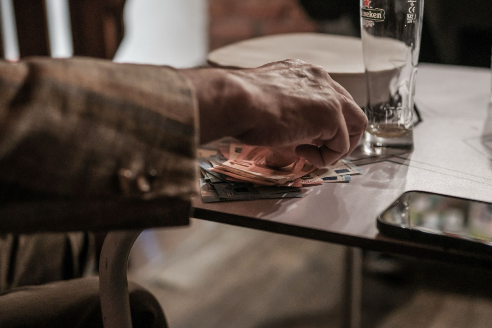 A hand resting on a stack of banknotes on a bar table beside an empty beer glass