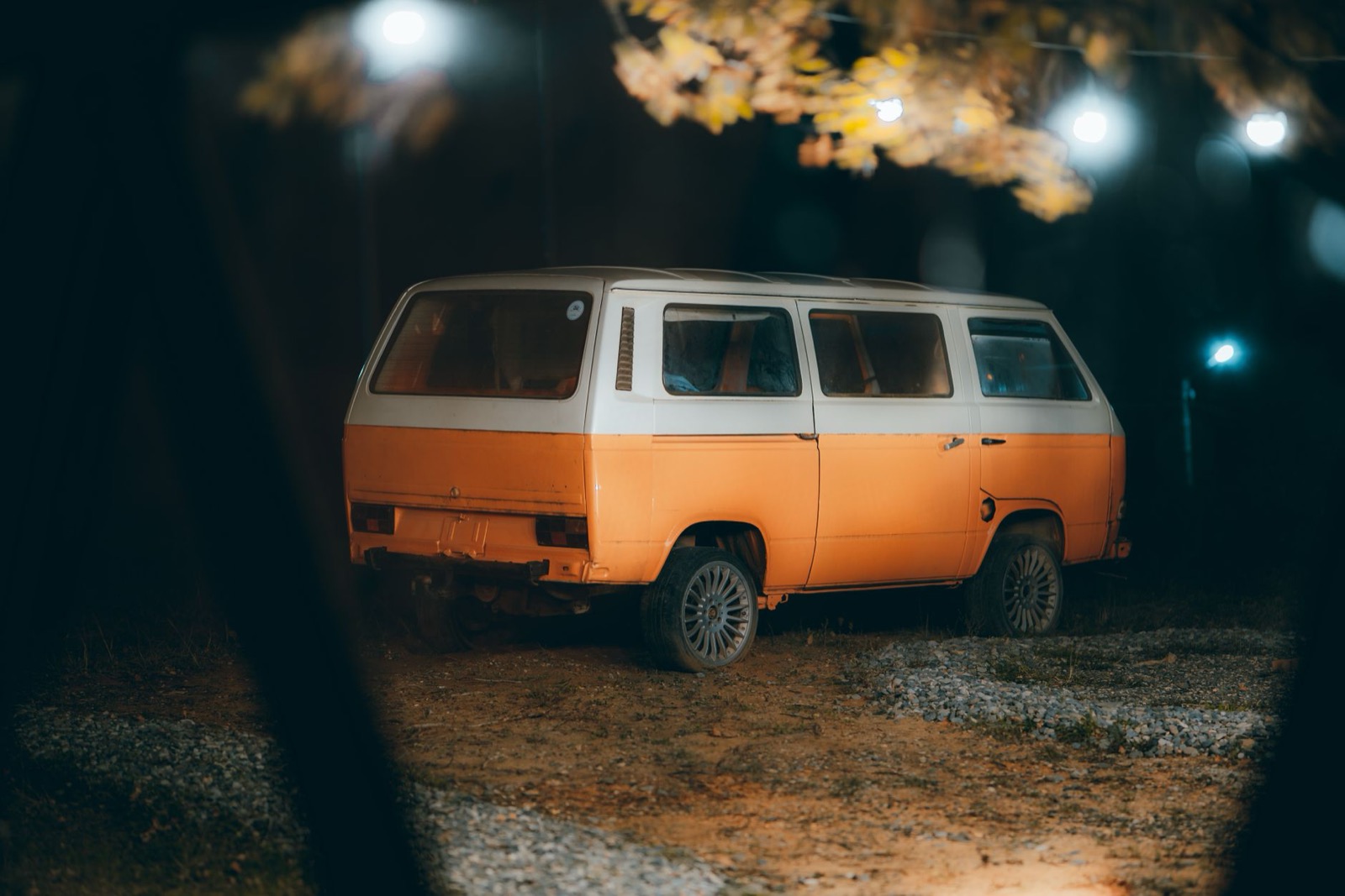 An orange and white van parked on gravel under trees at night with nothing set up outside