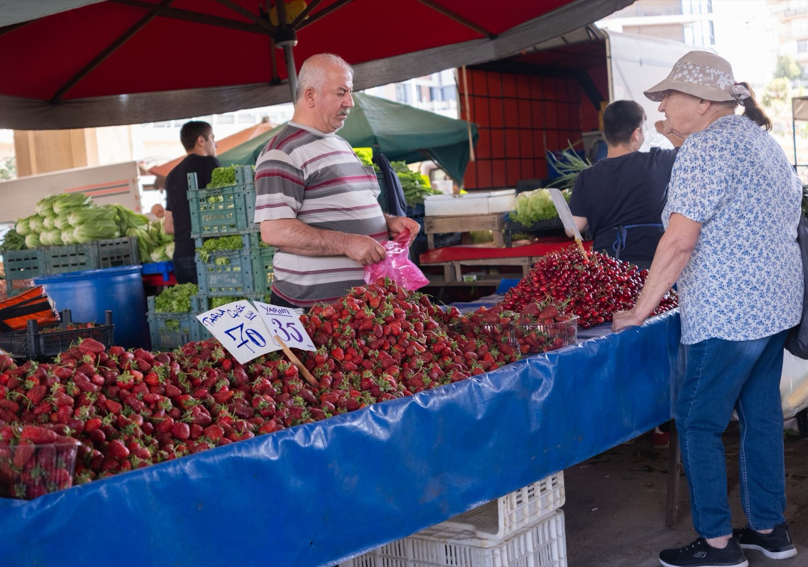A stallholder bagging strawberries for a customer across a market counter piled with fruit