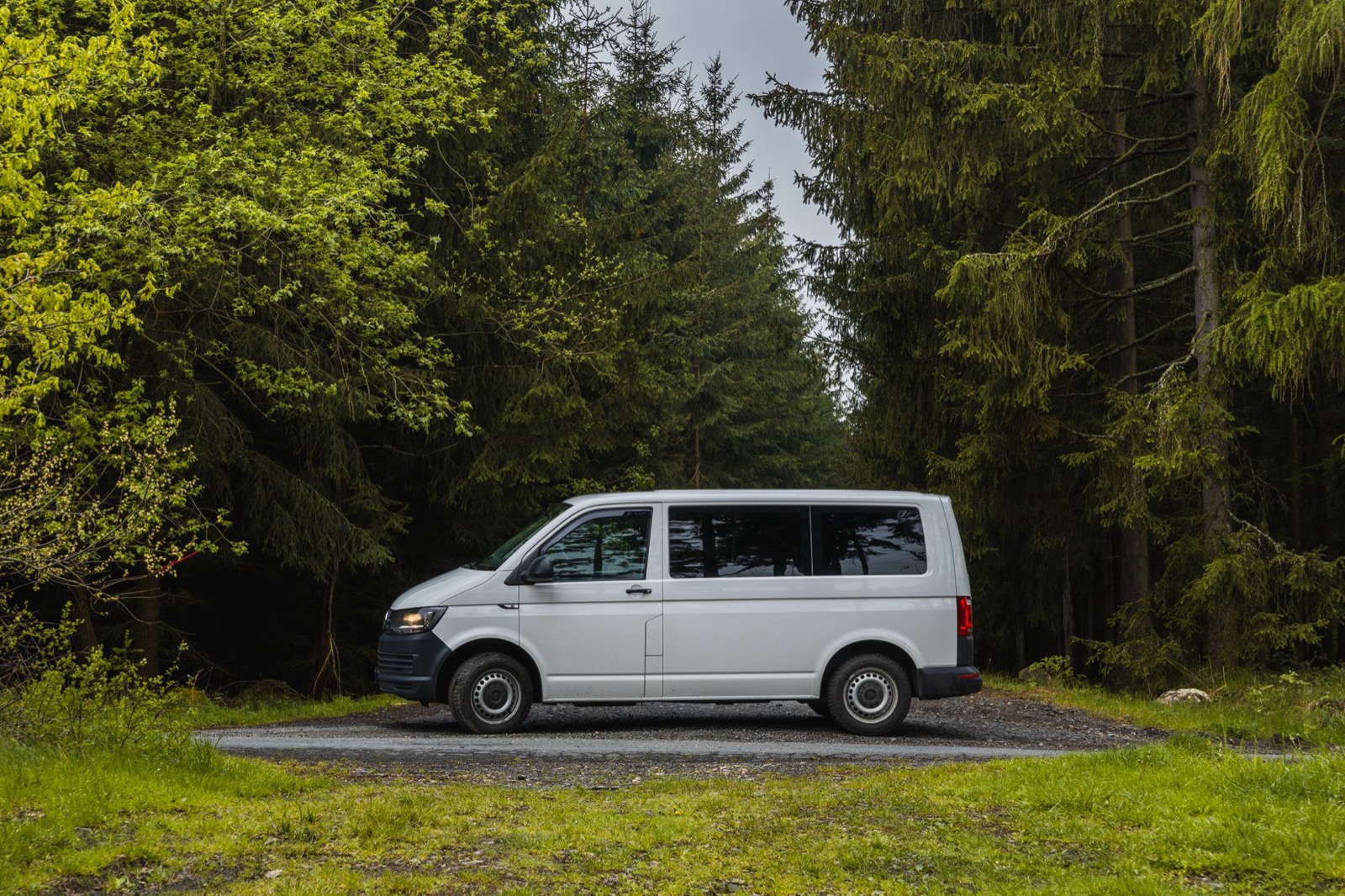 A white van parked on a gravel pull-in surrounded by spruce forest