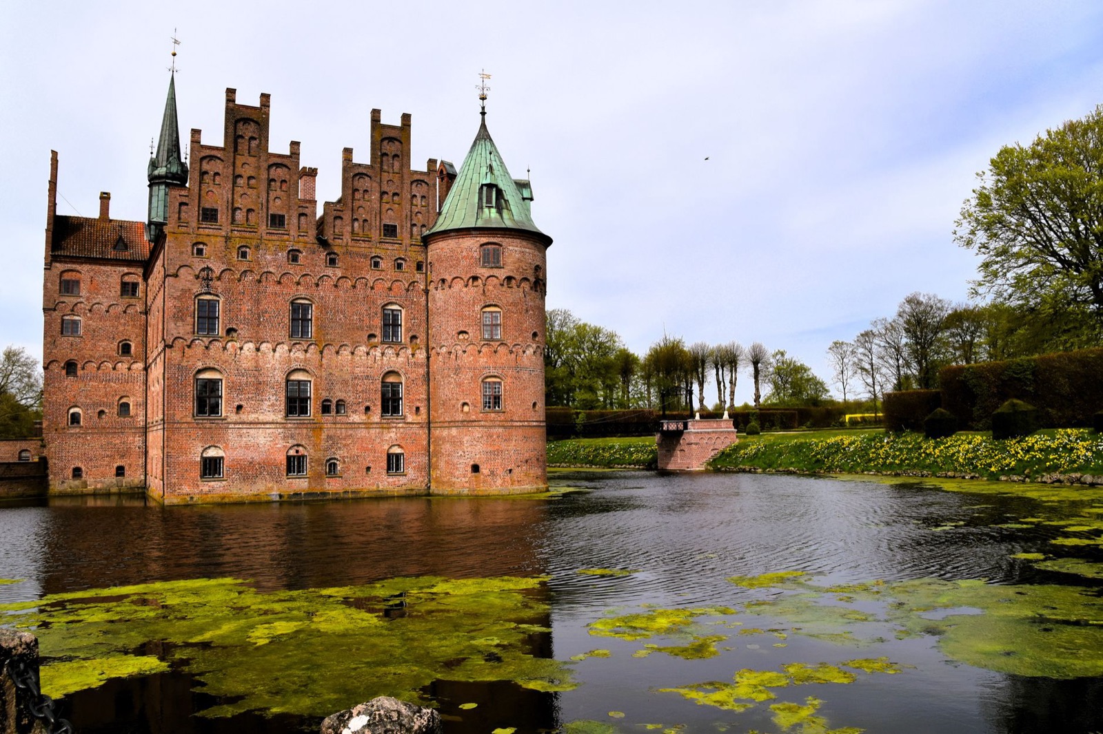 A moated Renaissance castle reflected in still water among trees on Funen