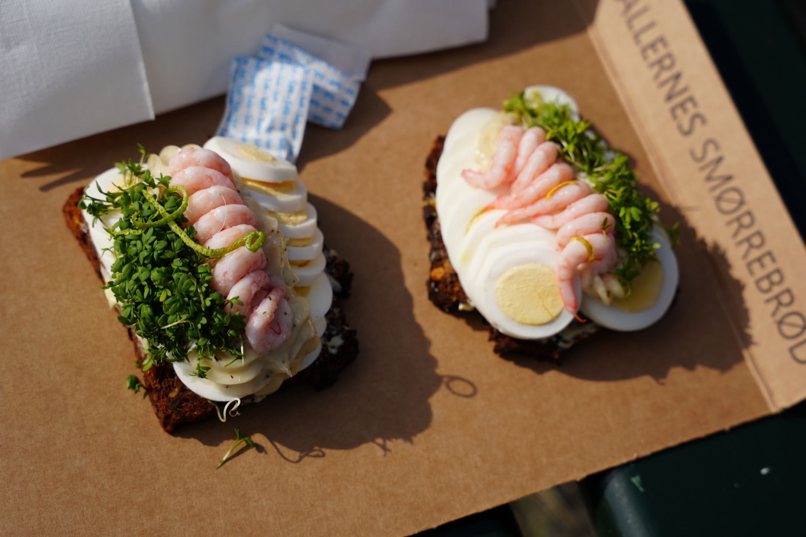 Two open rye sandwiches topped with prawns, sliced egg and cress on a paper tray