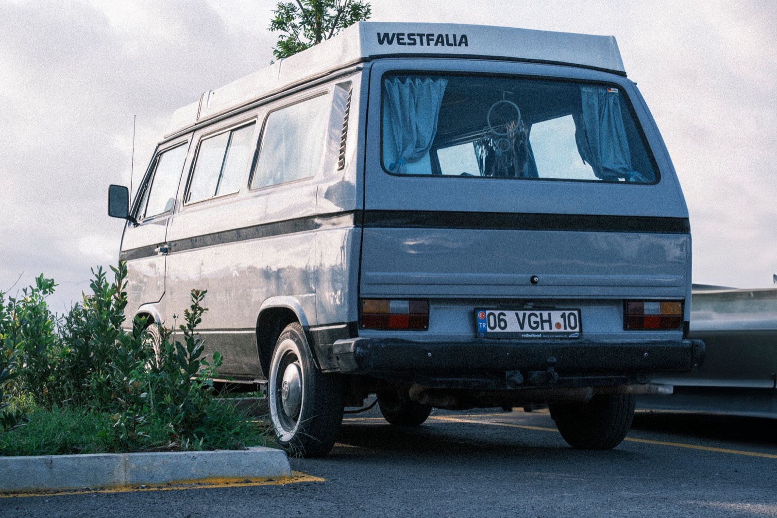 An old Westfalia camper van parked in a marked bay at the edge of a car park