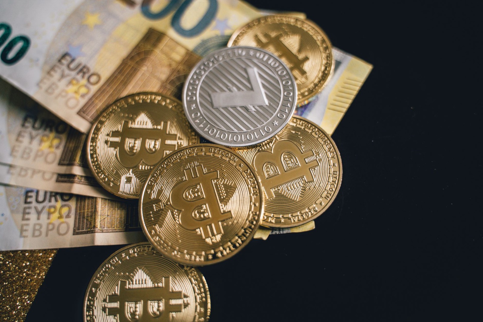 Euro banknotes under a pile of novelty bitcoin and ethereum coins