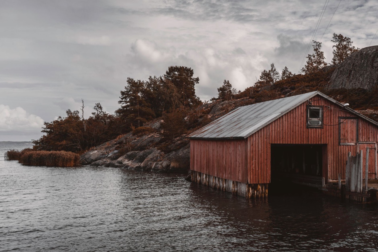 A red wooden boathouse on a rocky islet in the Finnish archipelago at dusk