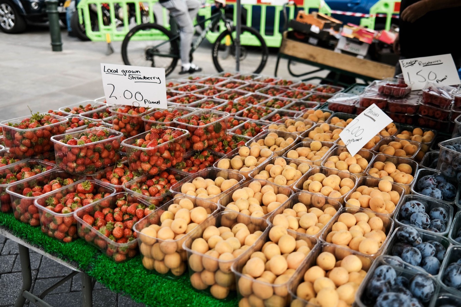 Punnets of strawberries, apricots and blueberries stacked on an outdoor market stall