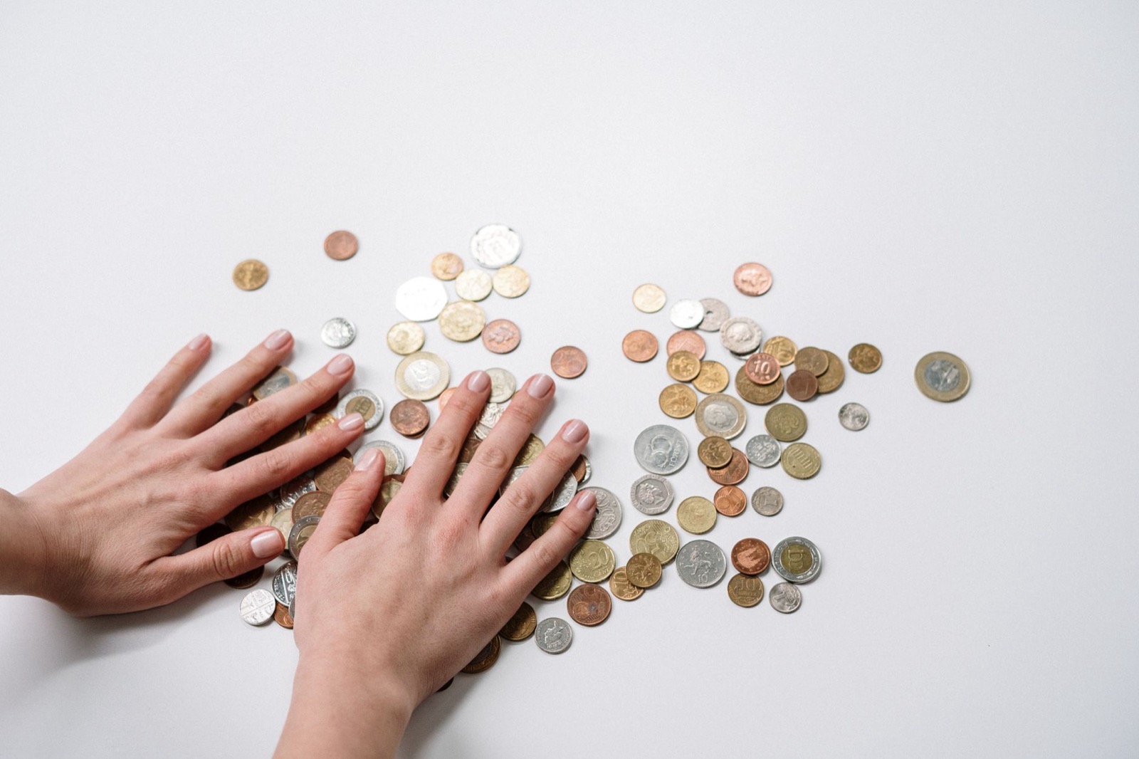 Two hands sweeping a scattered pile of loose coins across a white table