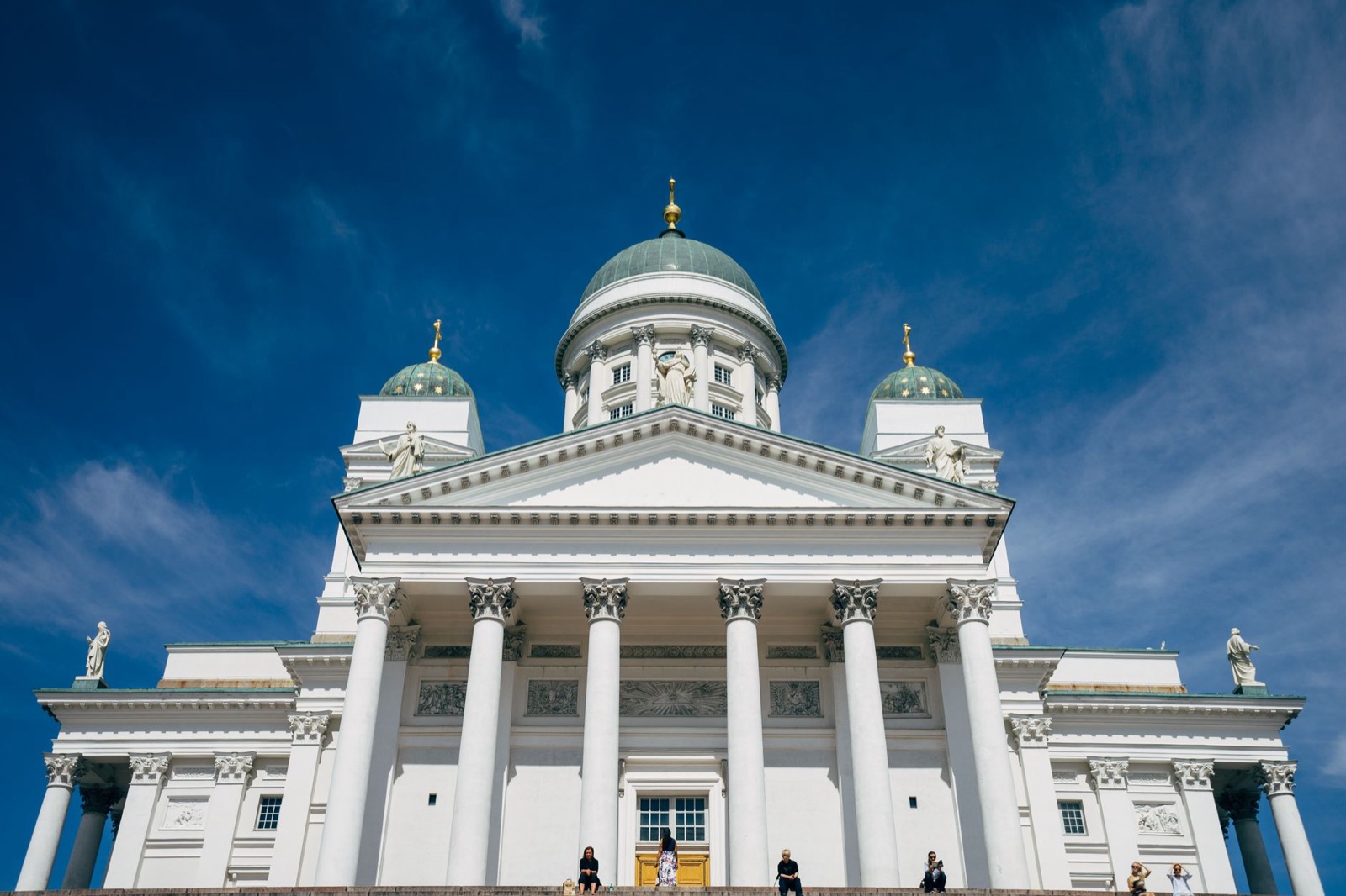 The white columns and green dome of Helsinki Cathedral against a deep blue sky