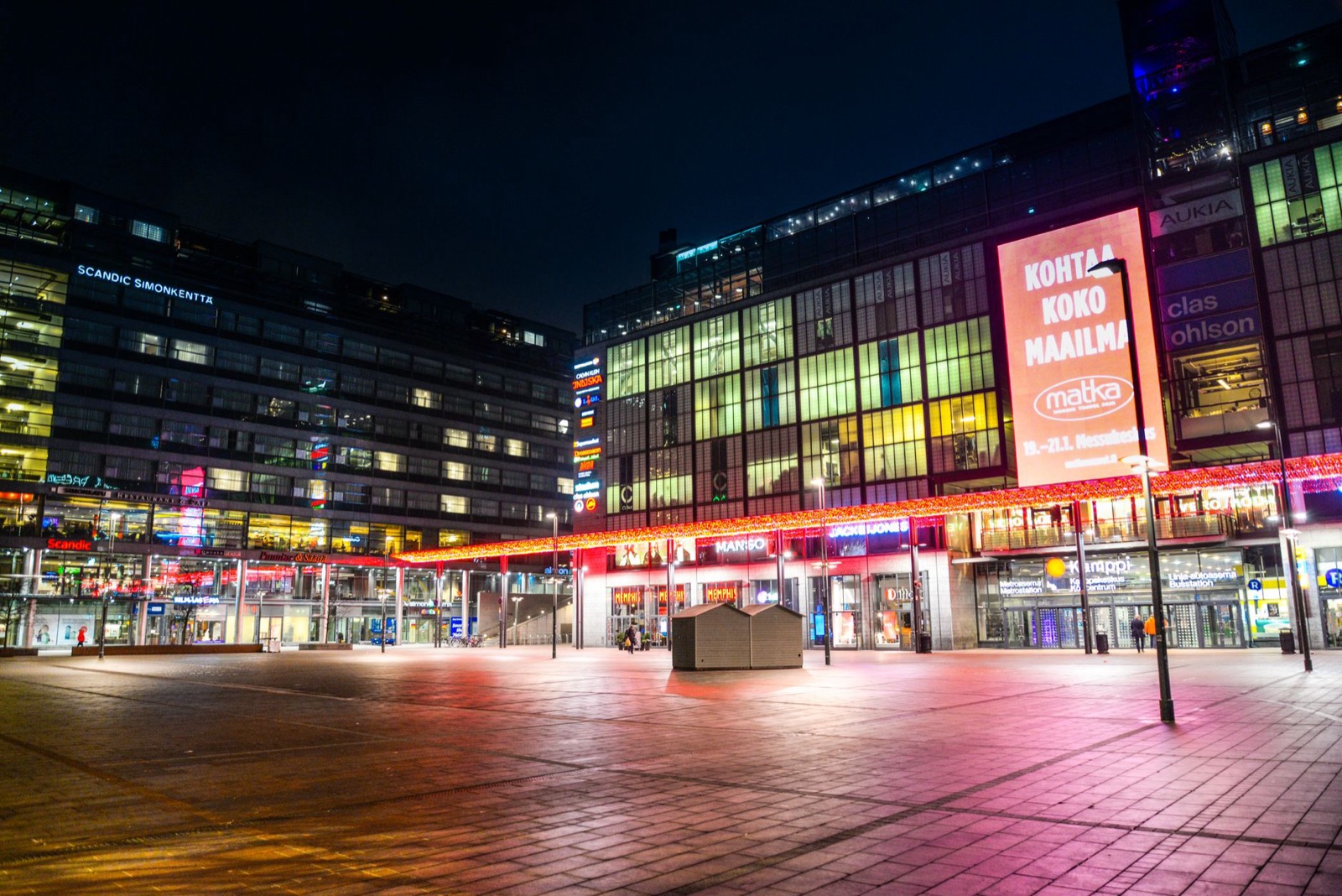 A lit shopping street and an empty paved square in central Helsinki at night