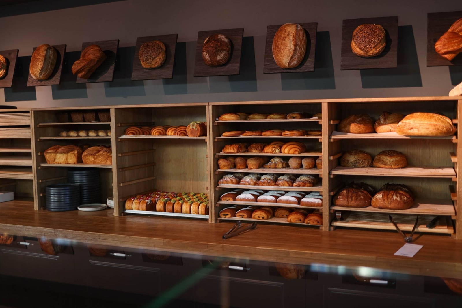 Wooden shelves of loaves and pastries behind a bakery counter, with more loaves mounted on boards along the wall above