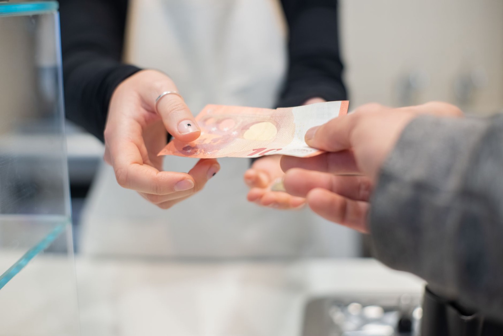 One hand passing a banknote to another across a shop counter