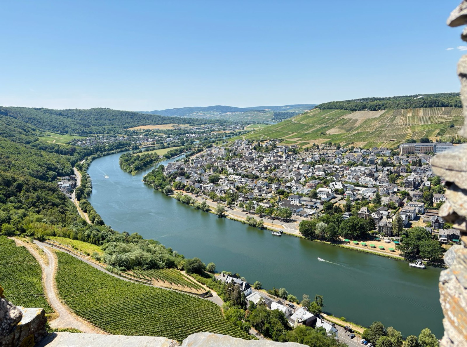 A bend in the Moselle seen from a castle wall, a slate-roofed town and steep terraced vineyards on the far bank