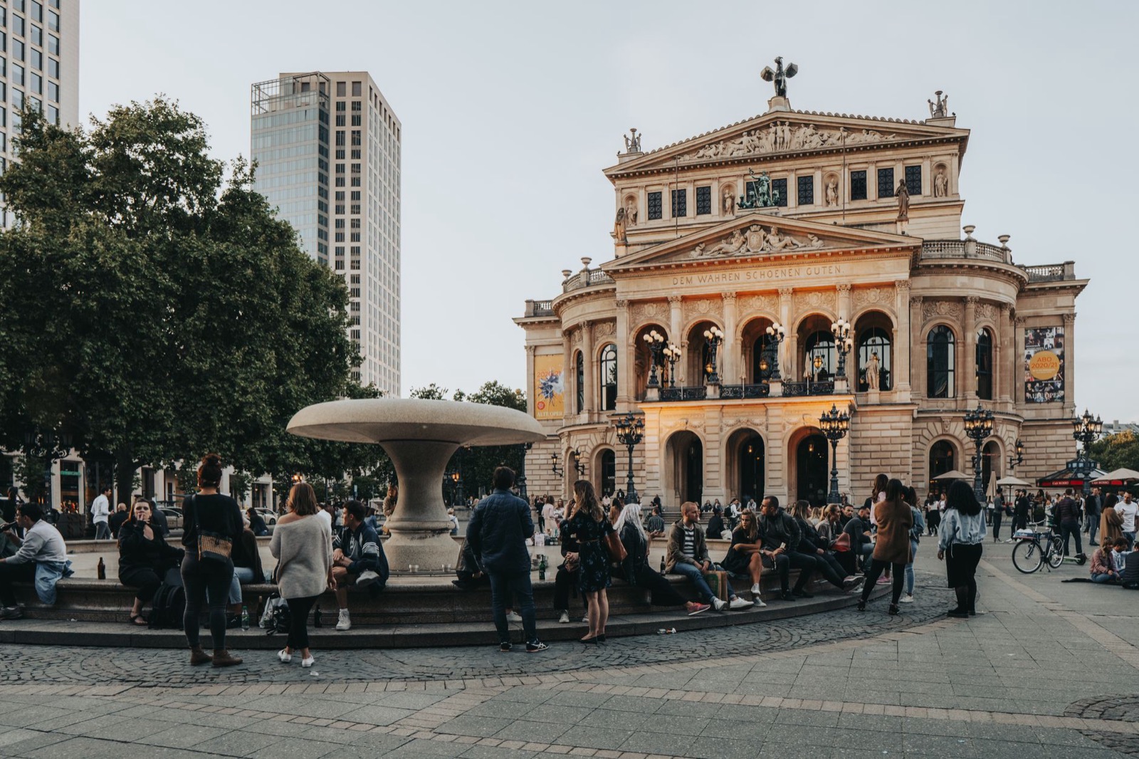 People sitting and standing around the fountain in front of the Alte Oper in Frankfurt on a summer evening