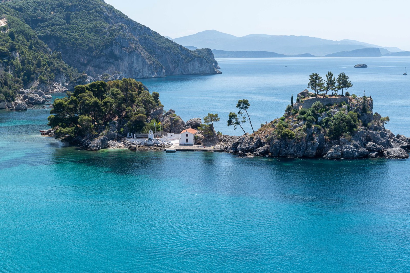 A wooded islet with a small white chapel on it, in a turquoise bay