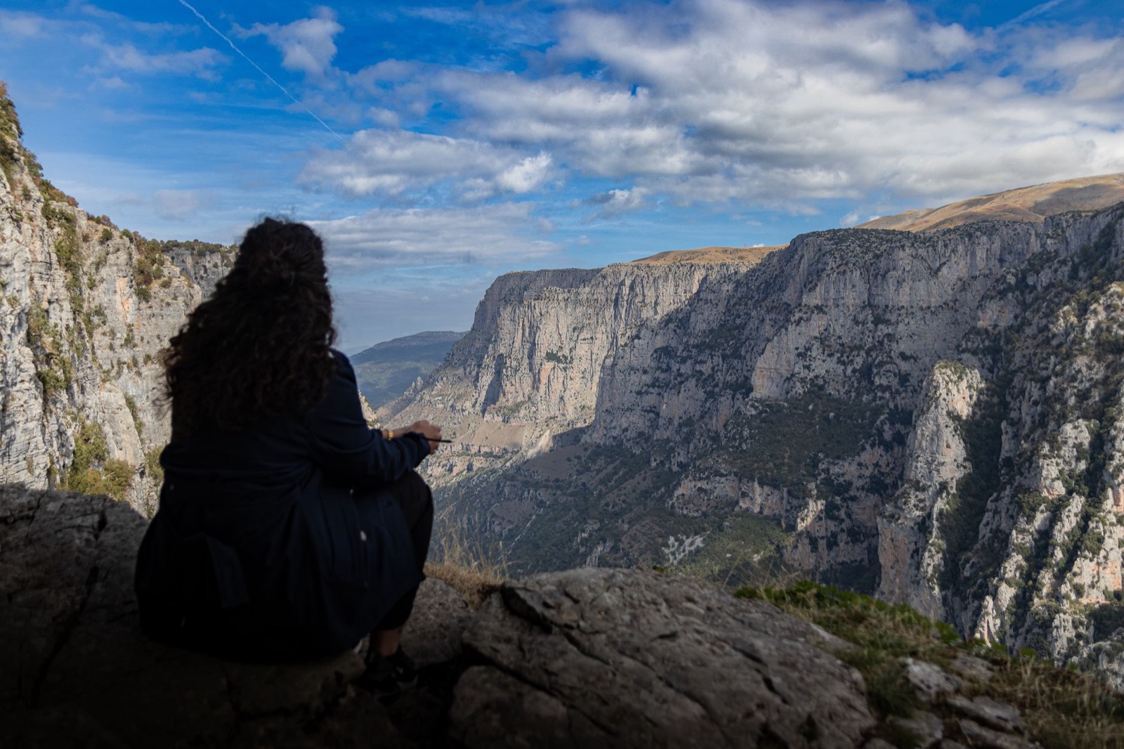 A walker sitting on the rim of a deep limestone gorge, looking across to the far wall