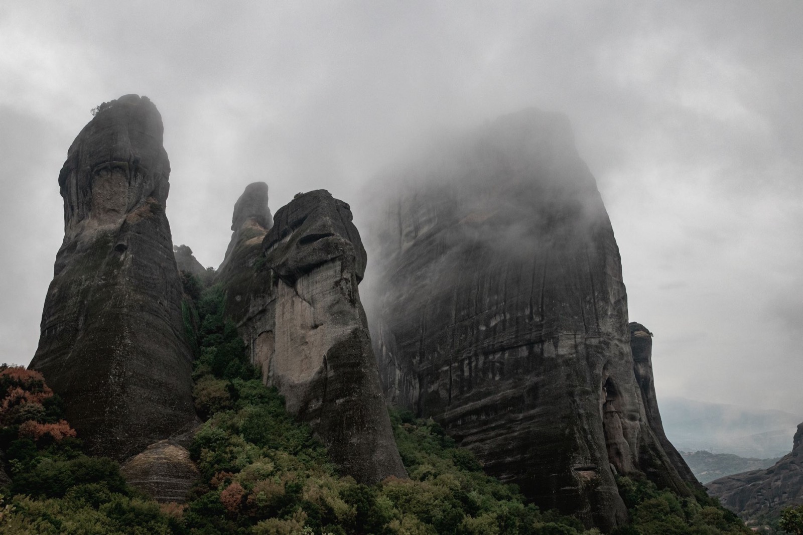 The rock pillars of Meteora rising into low cloud above wooded slopes
