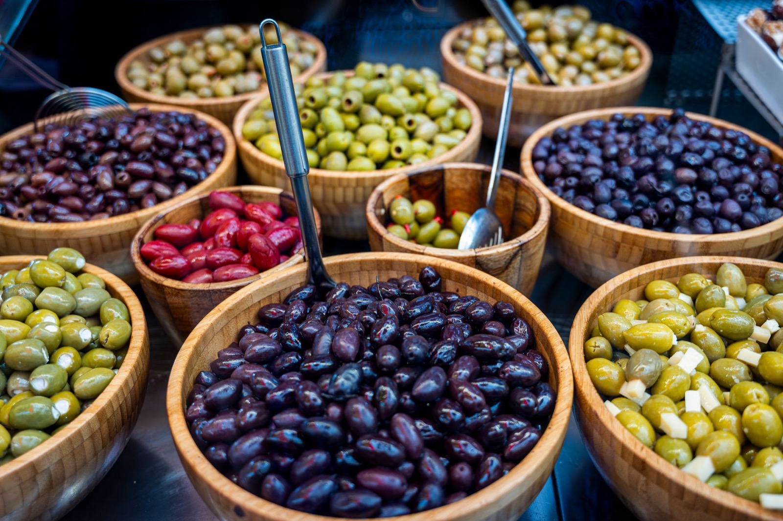 Wooden bowls of green, purple and stuffed olives on a market counter