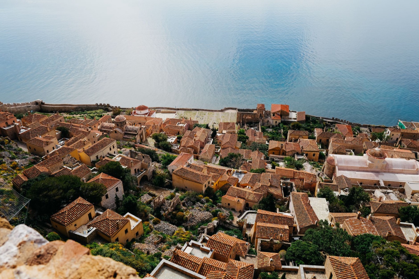 Tiled roofs of a walled stone town packed onto a ledge above the sea