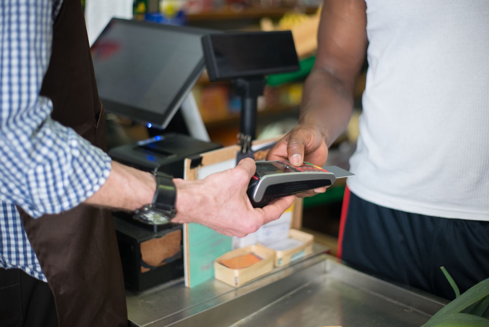 A customer holding a bank card to a handheld terminal at a shop counter
