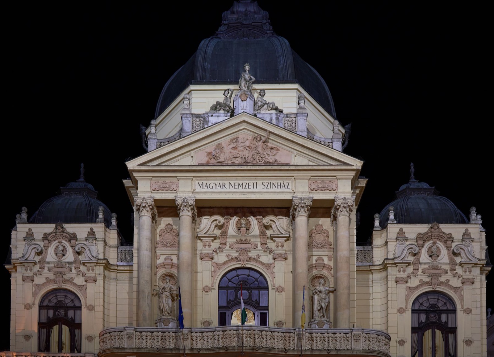 The floodlit facade and dome of a grand theatre at night, Magyar Nemzeti Színház carved above the columns