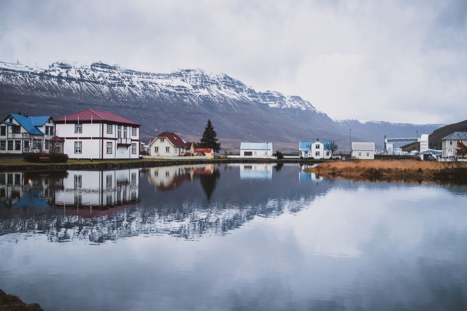 Coloured houses at the head of a fjord, reflected in still water below a snow-streaked ridge