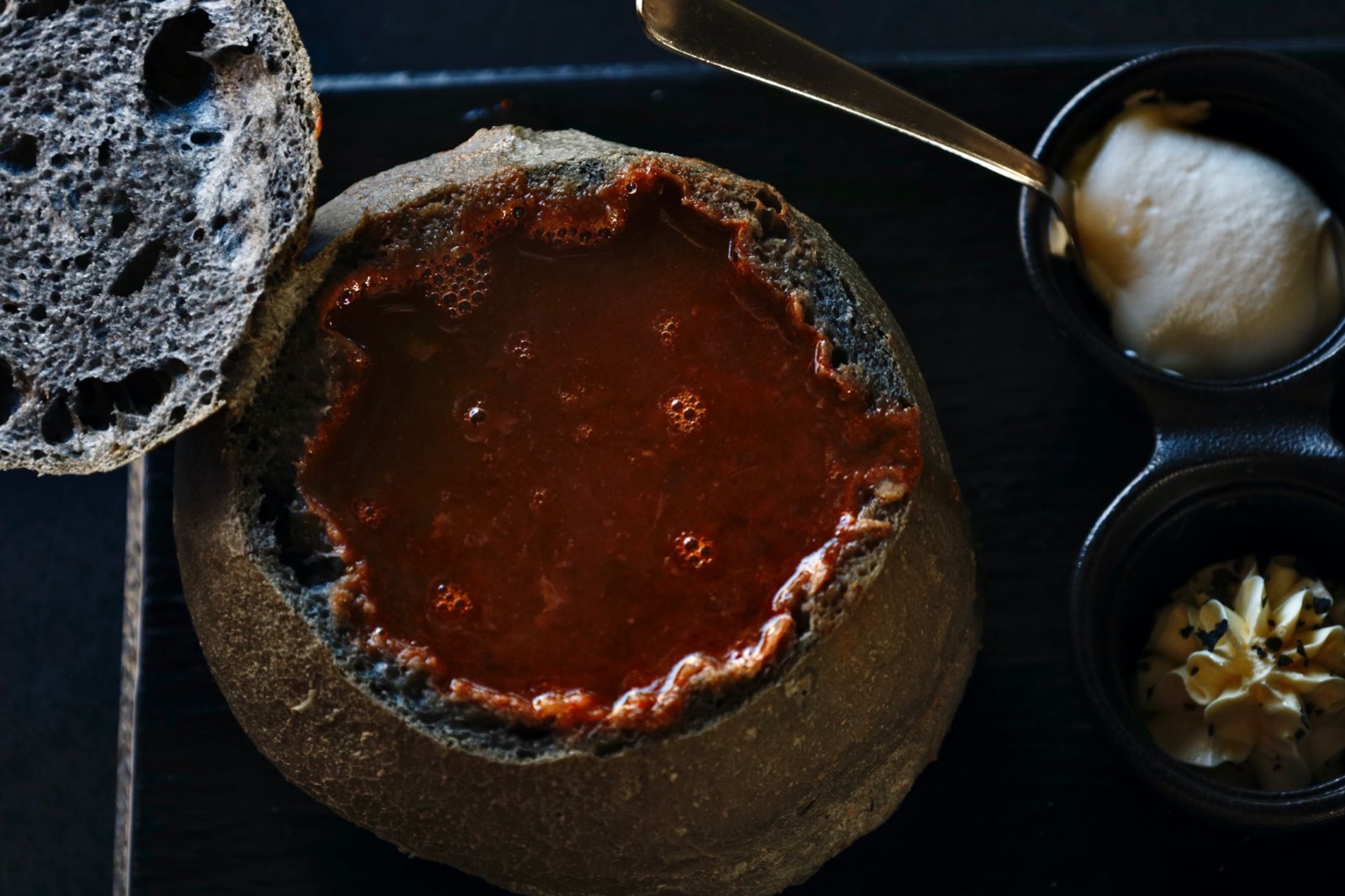 Red soup served in a hollowed loaf, with butter and sour cream in small dishes alongside