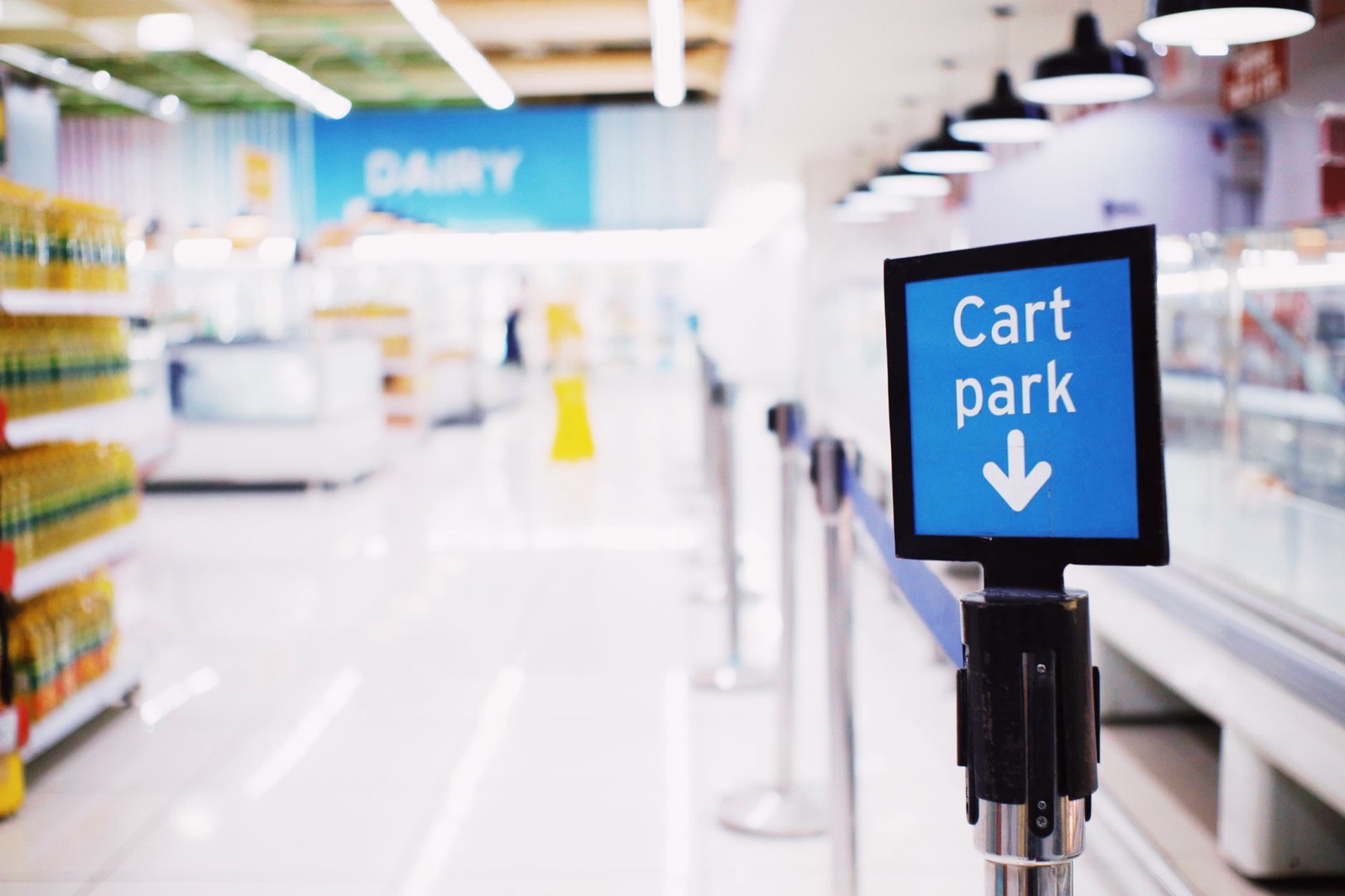 A bright supermarket aisle with a blue cart park sign in the foreground