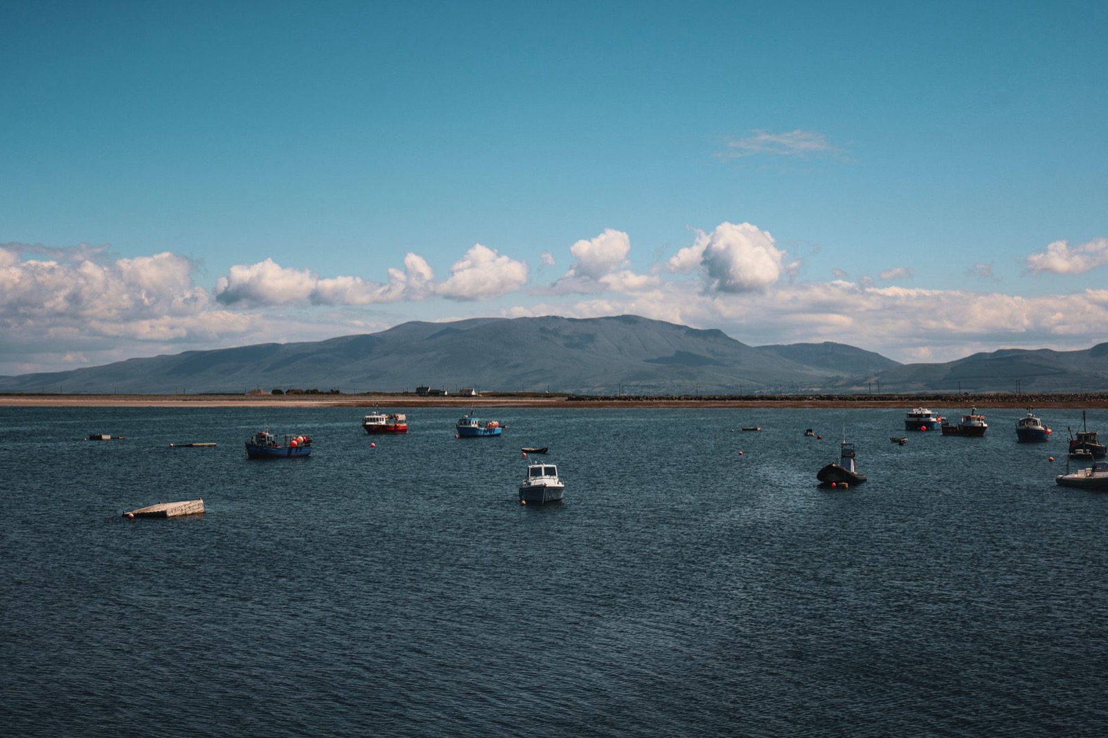 Small boats moored in a sheltered bay below low mountains under broken cloud