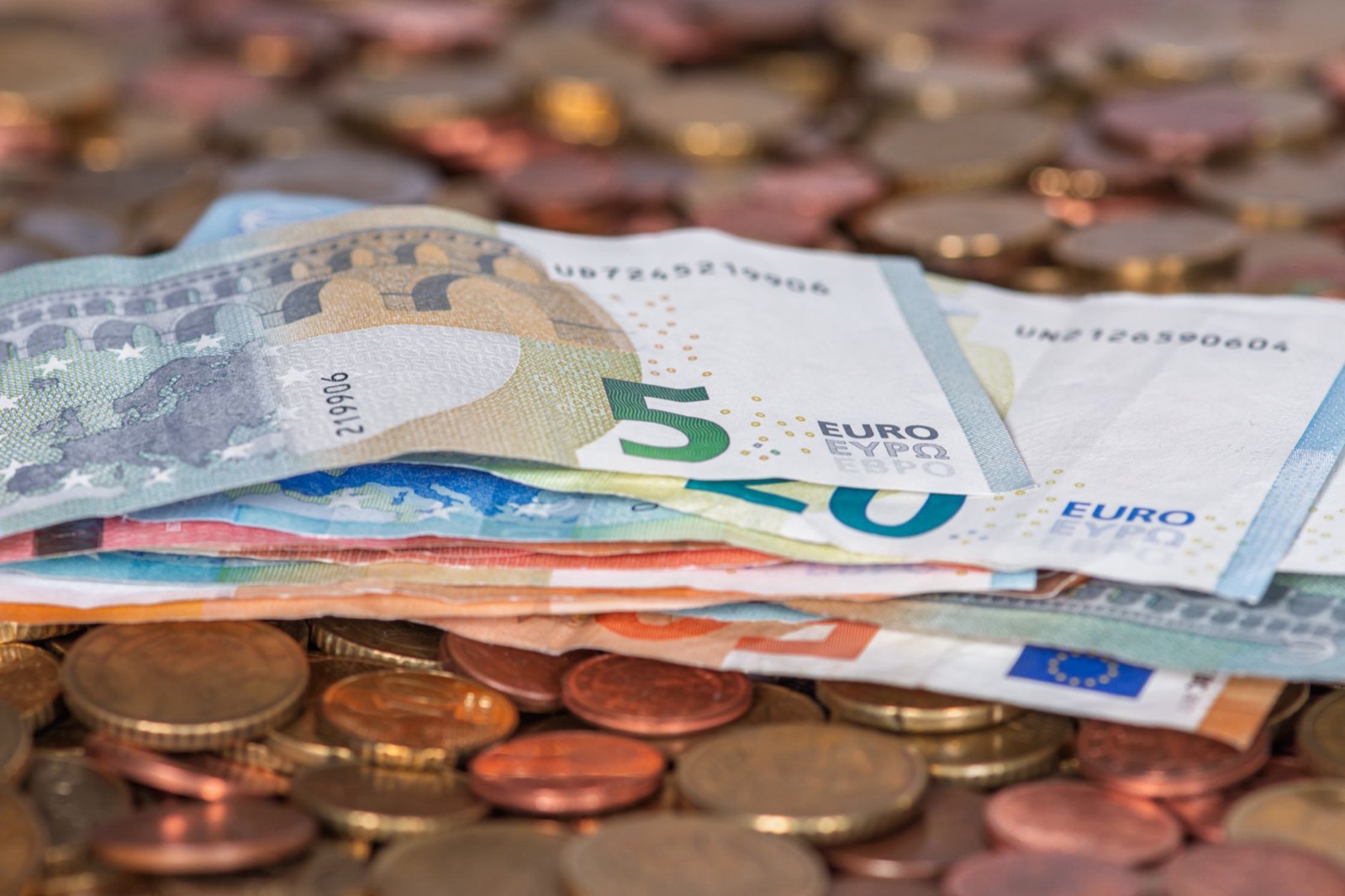 A stack of euro banknotes lying on a bed of loose coins