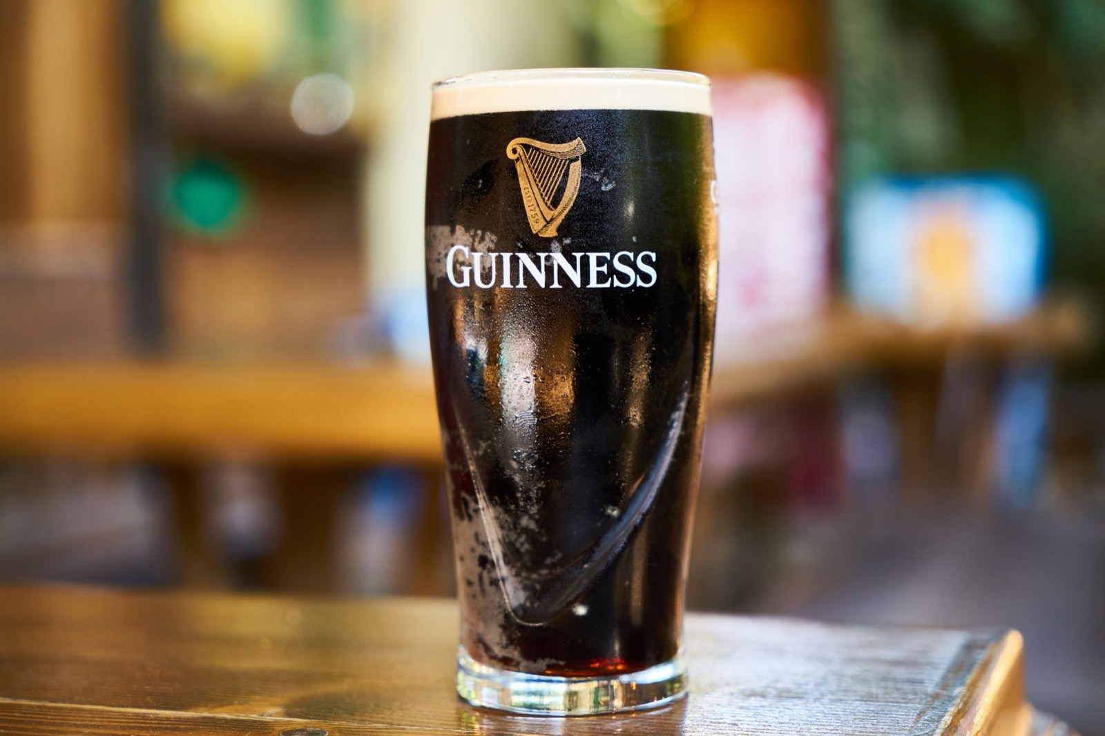 A settled pint of stout with a thick cream head on a wooden bar counter