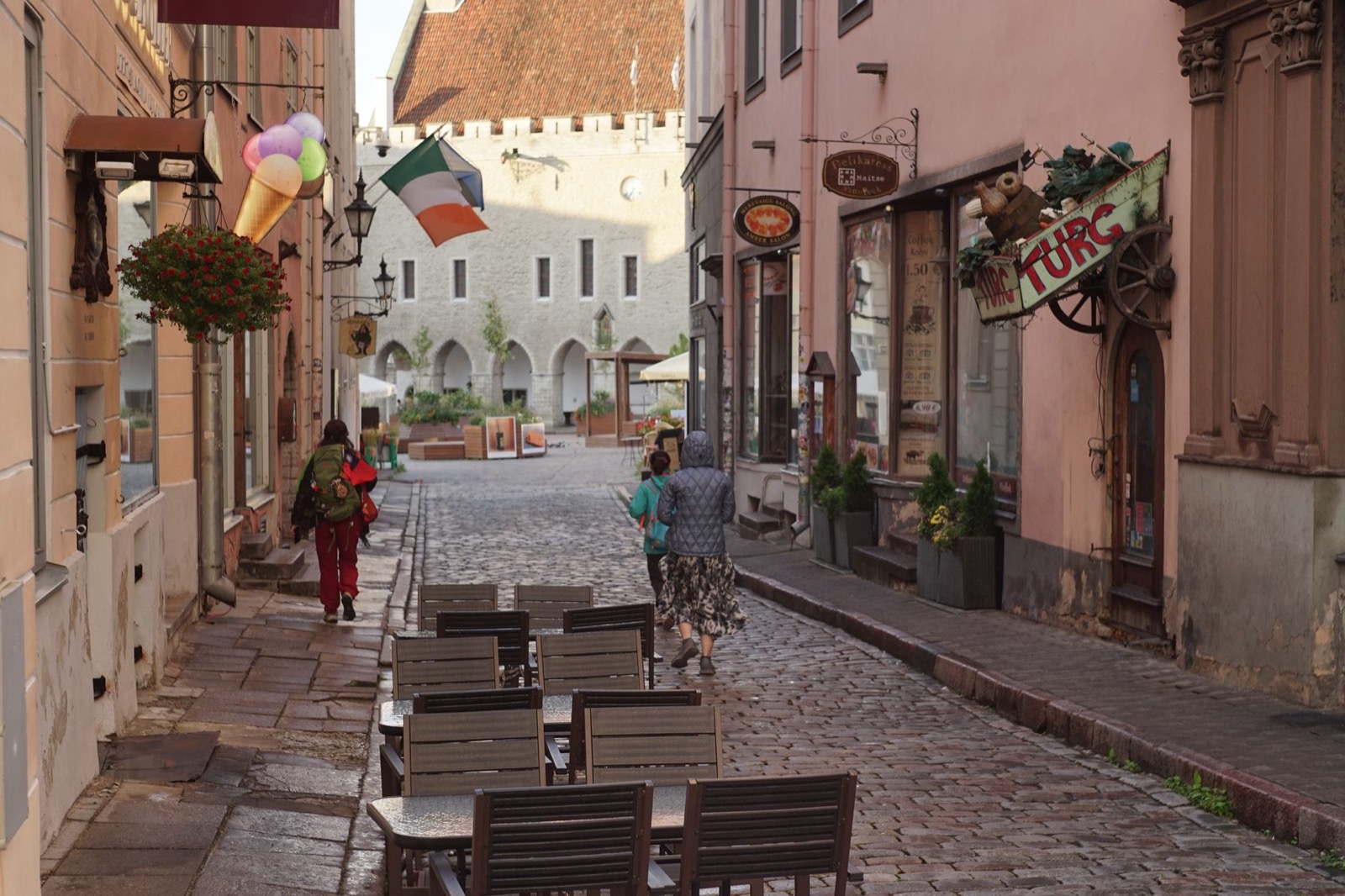 People walking a cobbled old town street lined with cafe tables and hanging shop signs