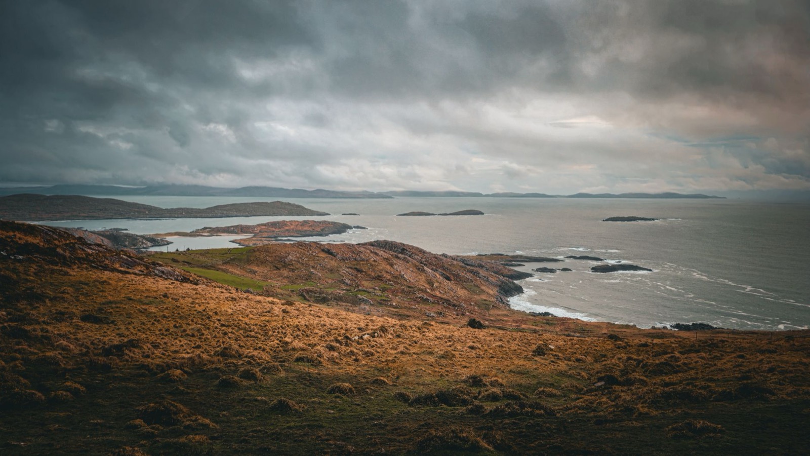 Heavy grey cloud over a bare brown headland and small islands on the Atlantic