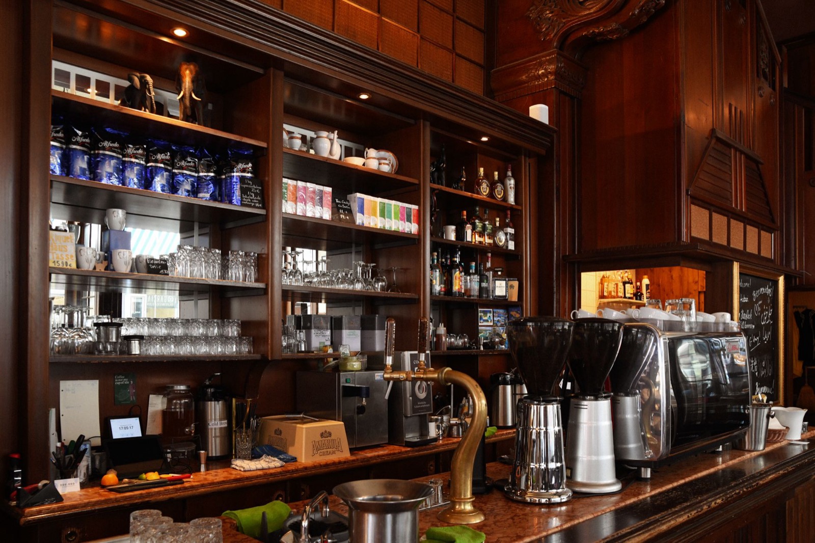 The dark wooden back bar of a cafe, glasses on mirrored shelves and an espresso machine along the counter