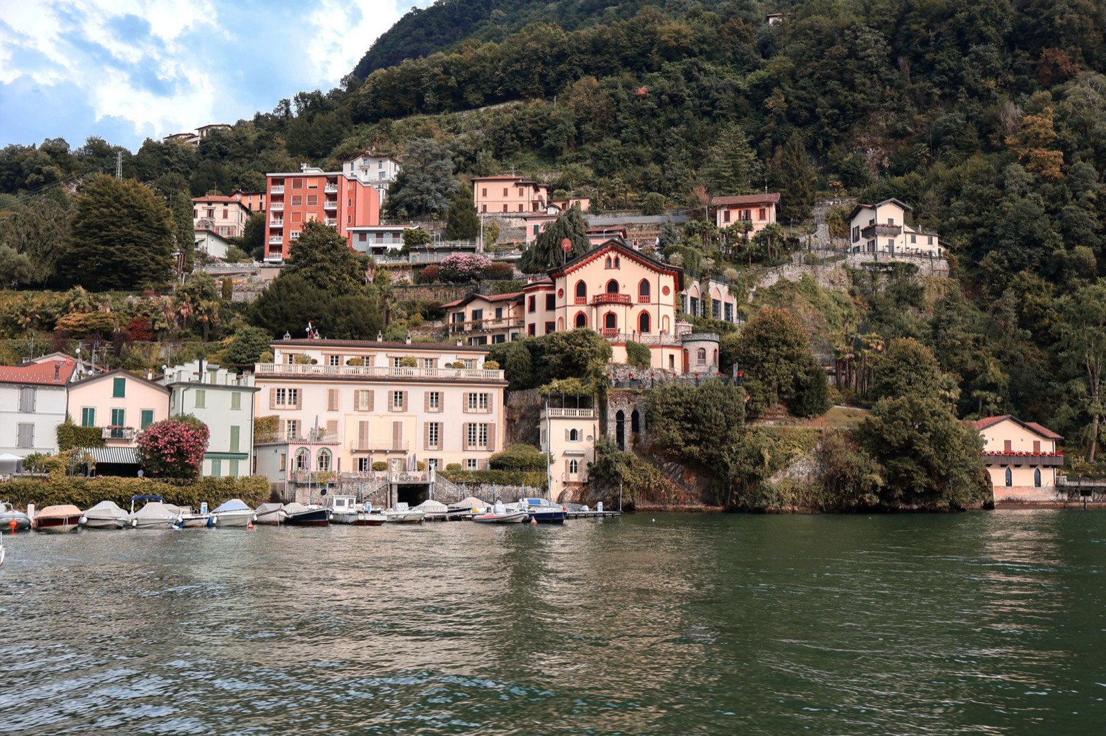 A lakeside village with pastel houses below steep wooded mountains on Lake Como