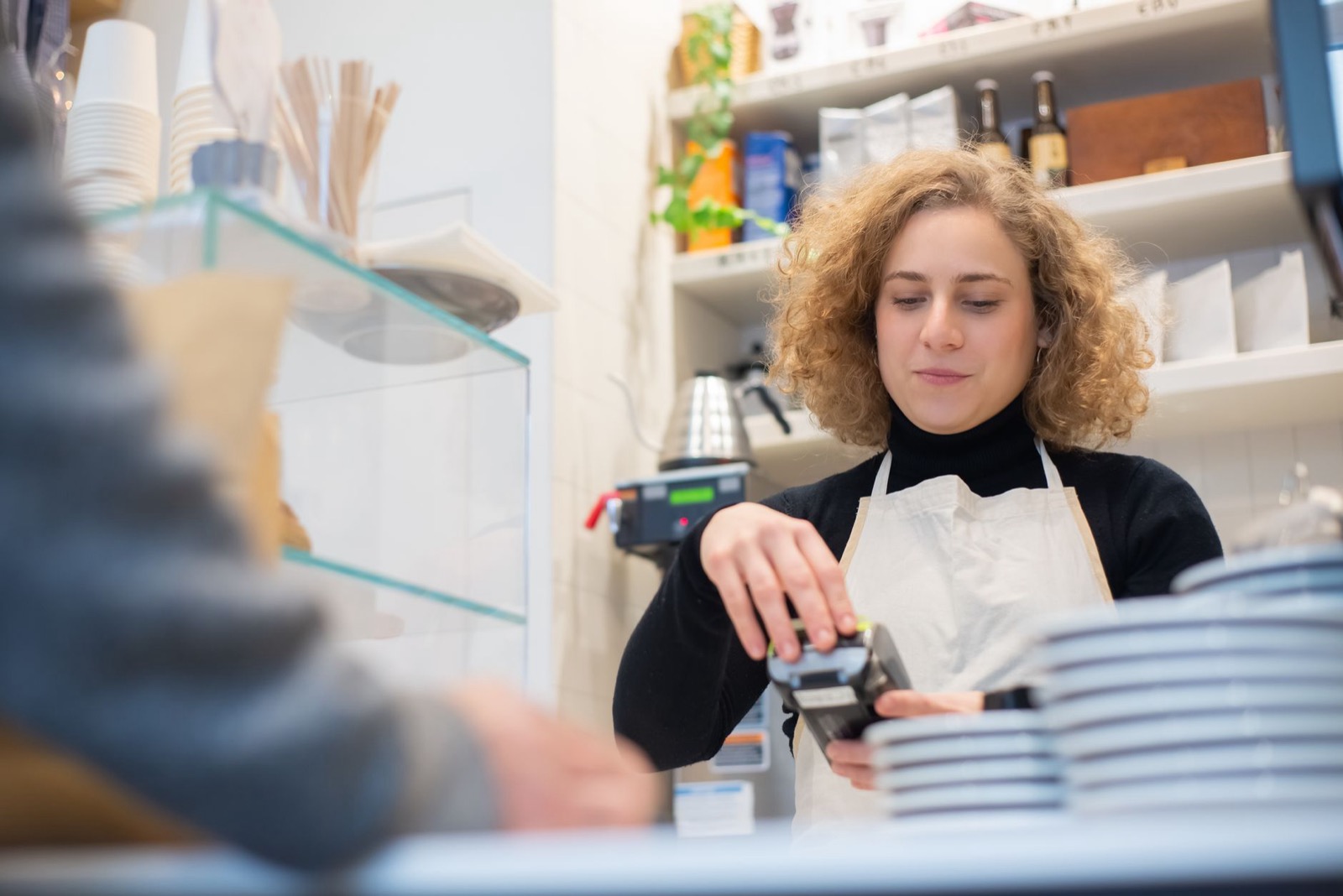 A barista in an apron holding a card reader out across a cafe counter