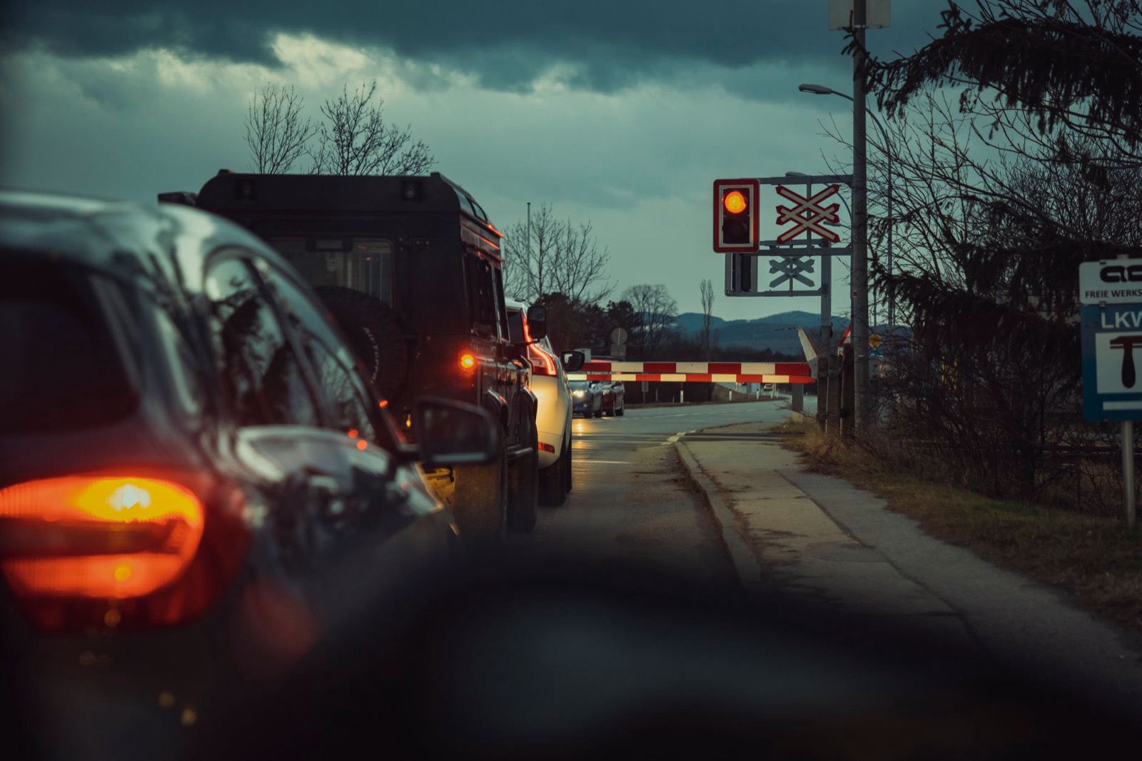 A queue of cars stopped at a lowered barrier under a red light at dusk, seen from inside a car